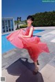 A woman in a pink dress standing by a swimming pool.