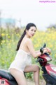 A woman sitting on a red scooter in a field of yellow flowers.