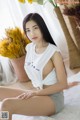 A woman sitting on top of a bed next to a vase of flowers.