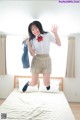 A woman in a school uniform jumping on a bed.